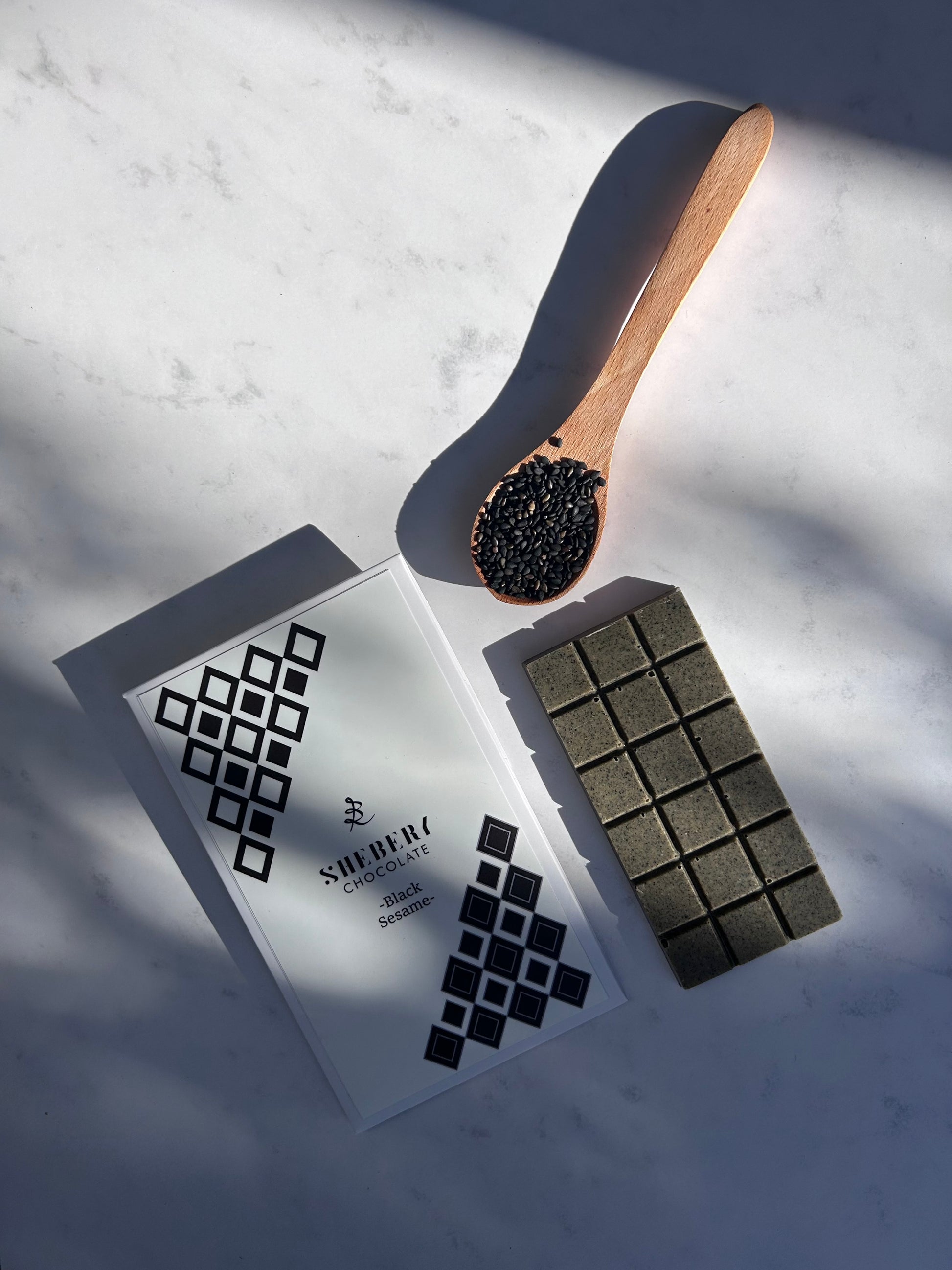 SHEBERYの黒ごまホワイトチョコレート“BLACK SESAME”。パッケージ、板チョコ、黒ごまを組み合わせた無添加のクラフトチョコで、美容と健康を意識した毎日のおやつにも。
